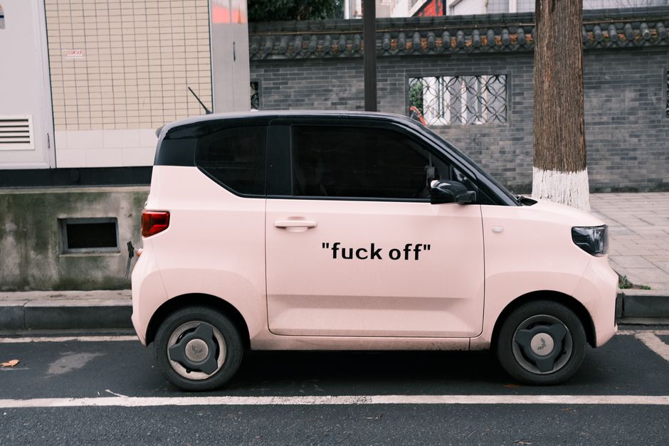 Side view of a pink compact electric vehicle parked on an urban street with bold text on the side.